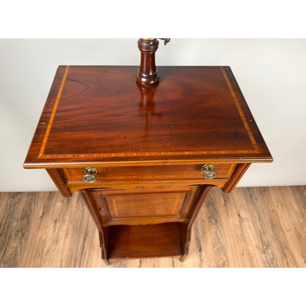 A high-angle view of an Antique English Mahogany Inlaid Shaving Stand with Adjustable Mirror, c. 1880–1900, featuring a drawer with two brass pulls, a small cabinet door, an open shelf, and an adjustable mirror mount on the tabletop.