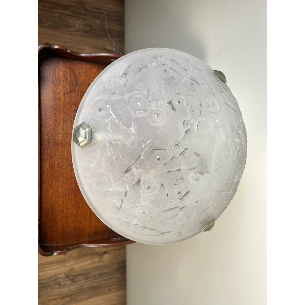 A Vintage French Art Deco frosted glass table lamp by Muller Frères Lunéville (c.1920), featuring geometric etching and three metal fasteners, rests on wood before a pale wall—a timeless classic.