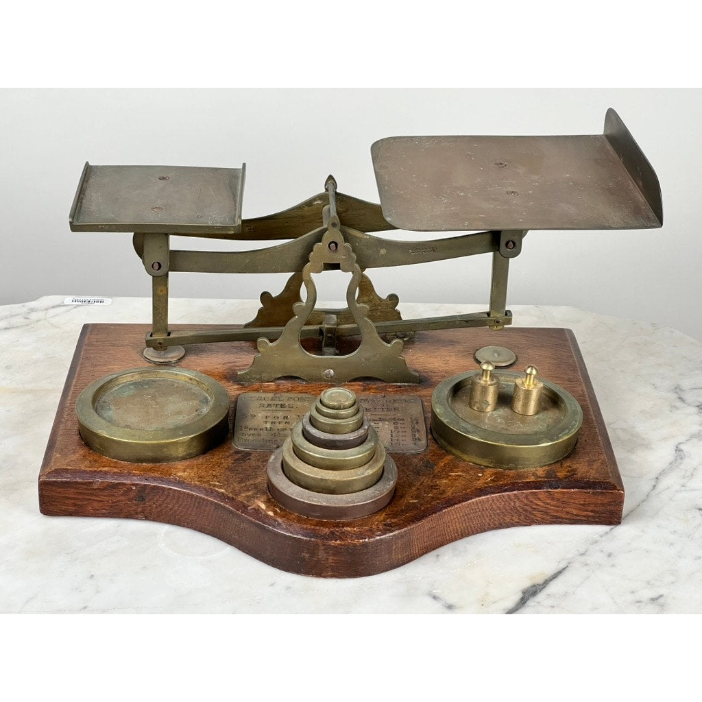 The Antique 19th Century English Postal Scale features two weighing pans, stacking brass weights, and a wooden base, elegantly displayed on marble—a striking example of antique scientific craftsmanship.