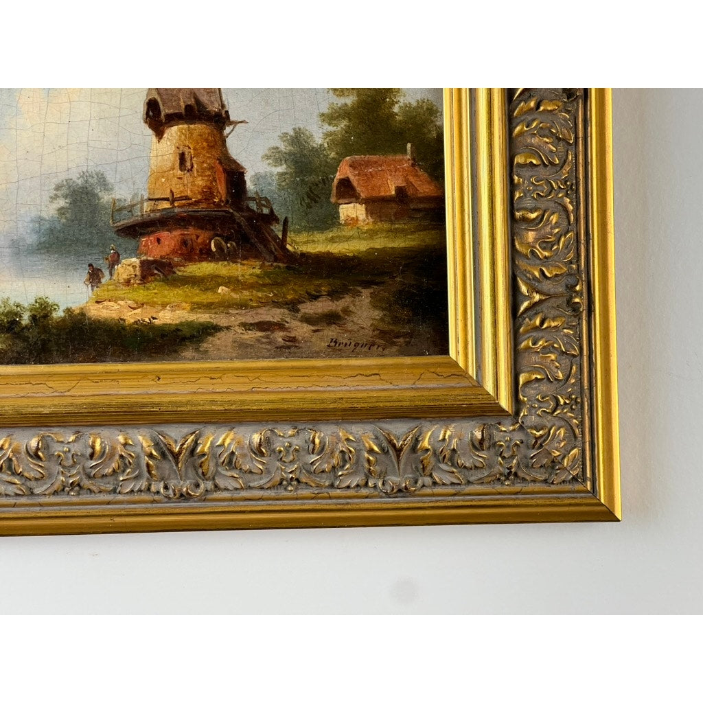 Close-up of an ornate gold frame detailing part of an Antique Continental School oil-on-canvas landscape, signed “Brüguer” (circa 1880-1910), showing a rustic windmill, greenery, and a small house beneath a blue sky.