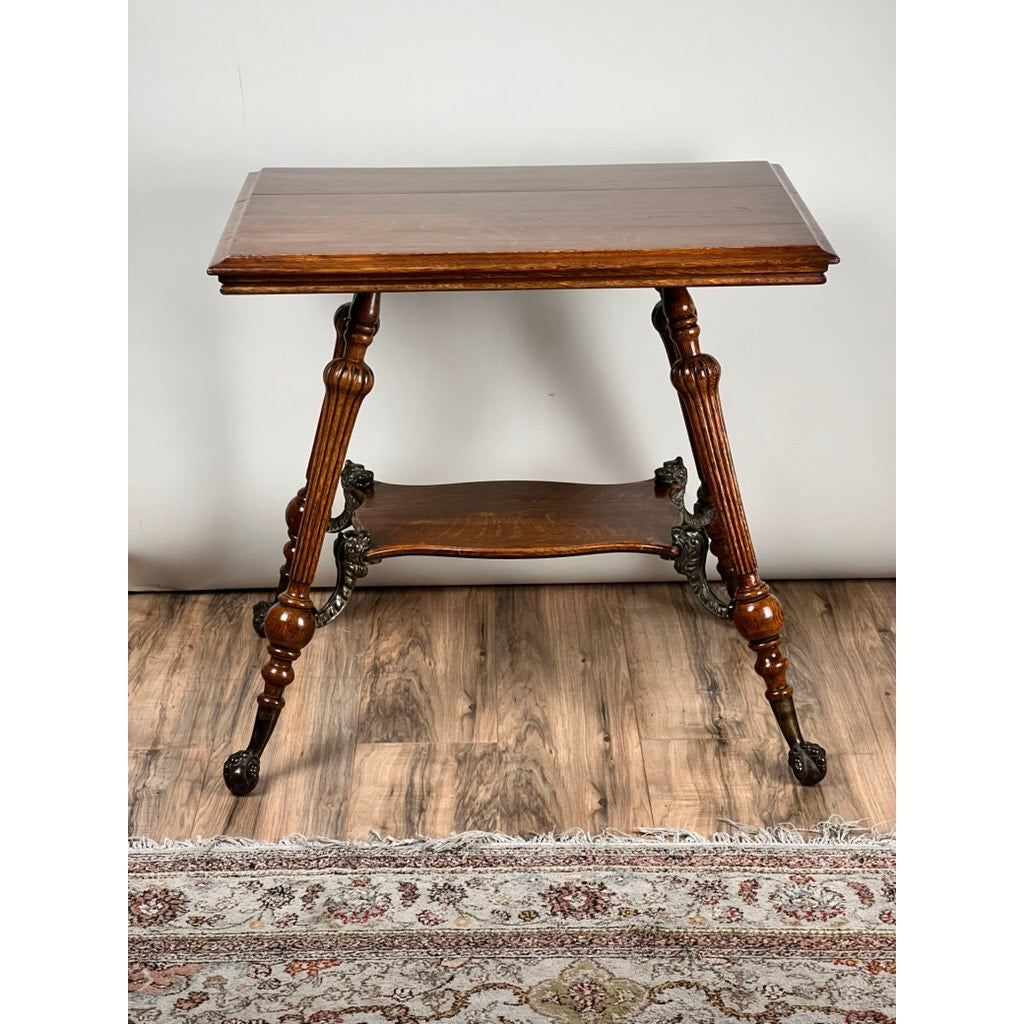 An Antique Victorian Oak Lamp Stand with Bronze Lions Head Mountings (late 19th century) stands on a wooden floor beside a patterned rug, featuring ornate legs, a rectangular top, lower shelf, and decorative feet.