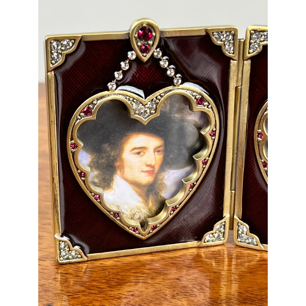A New in Box Jay Strongwater Bejeweled Enamel Double Heart Picture Frame with gold trim and jeweled accents is displayed on a wooden surface.