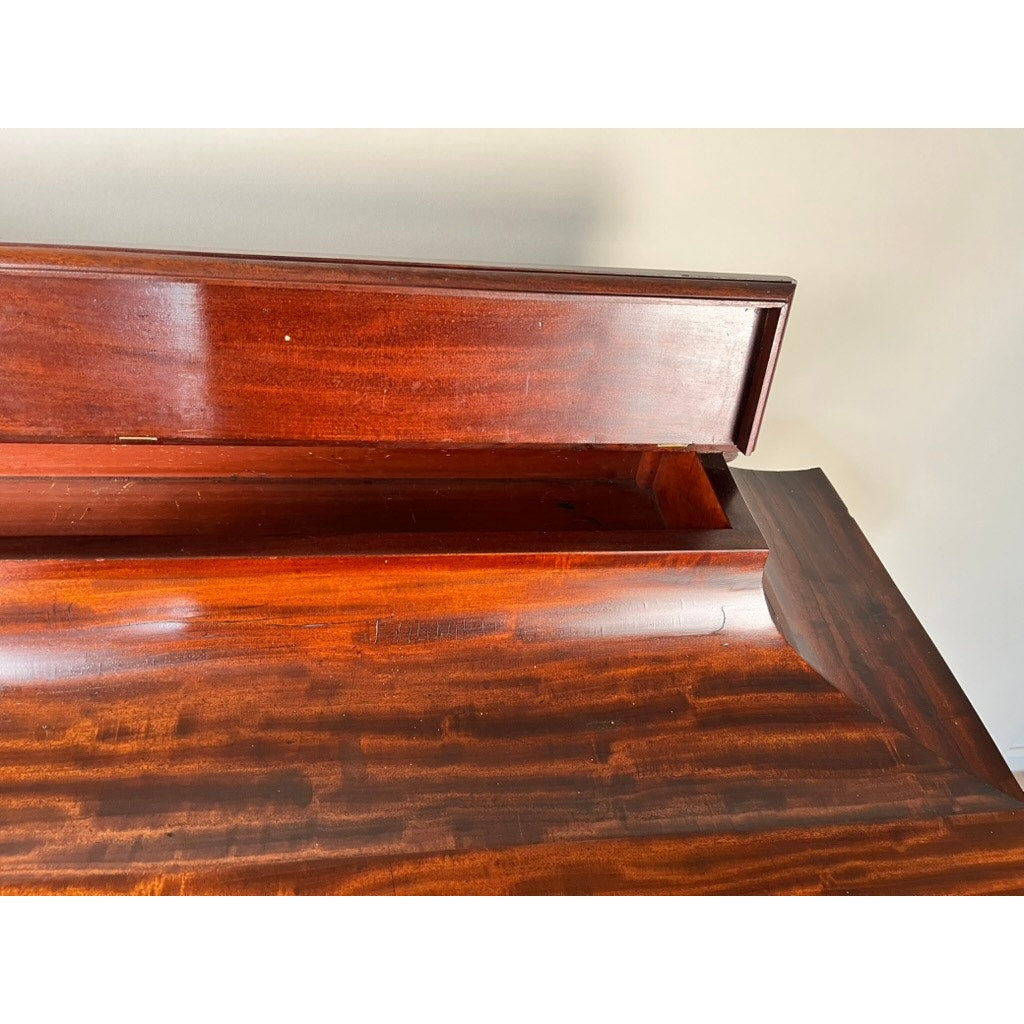 A close-up of an Antique American Empire Albany Four Drawer Chest c. 1840, featuring a rich reddish-brown finish, visible grain patterns reminiscent of classic flame mahogany, and an open rear compartment revealing hidden storage. Brand unknown.