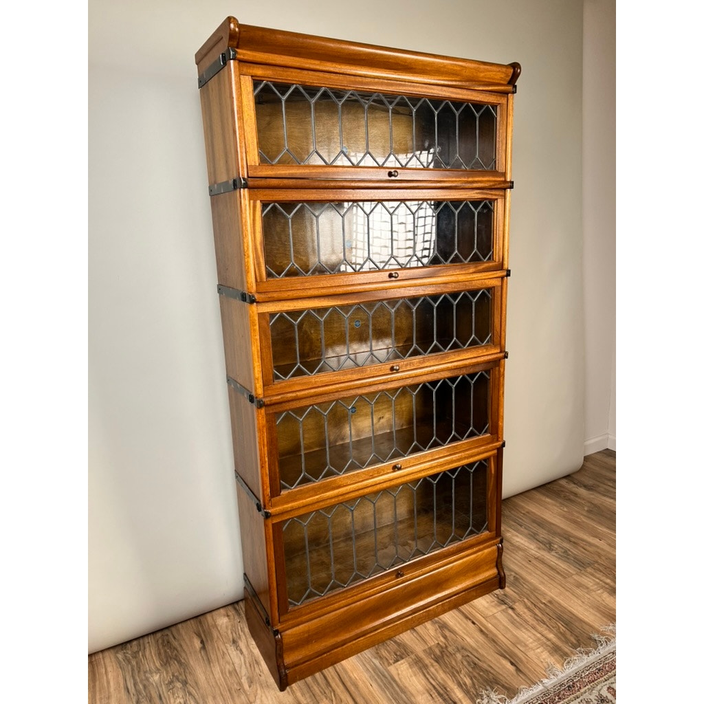 A Vintage Globe Wernicke Leaded Glass Five Stack Barrister Bookcase by Globe Wernicke, featuring modular sections and elegant leaded glass doors, stands on a wood floor against a plain light-colored wall.