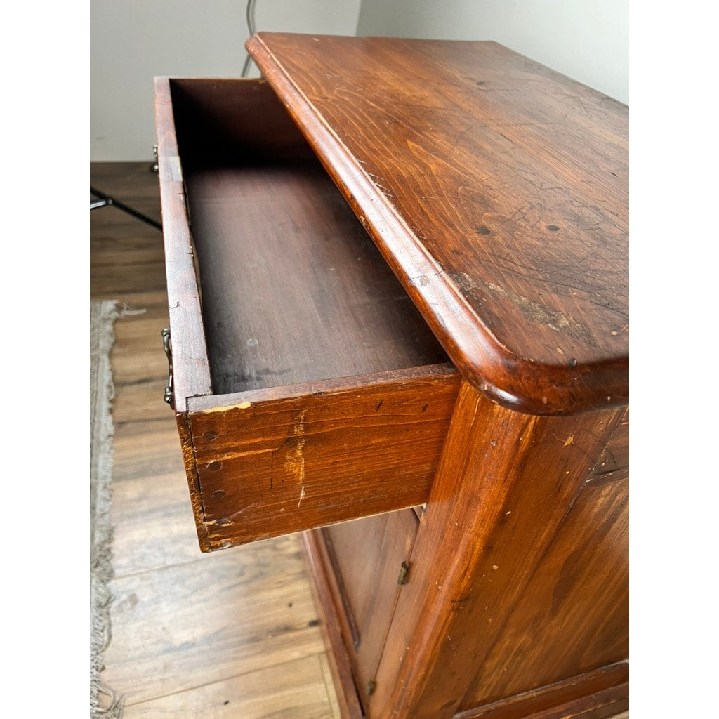 A close-up of an Antique Victorian Pine Commode c. 1900 with an open top drawer, displaying surface scratches and wear. The piece stands on a wooden floor beside part of a woven rug. Brand: None and/or Unknown.