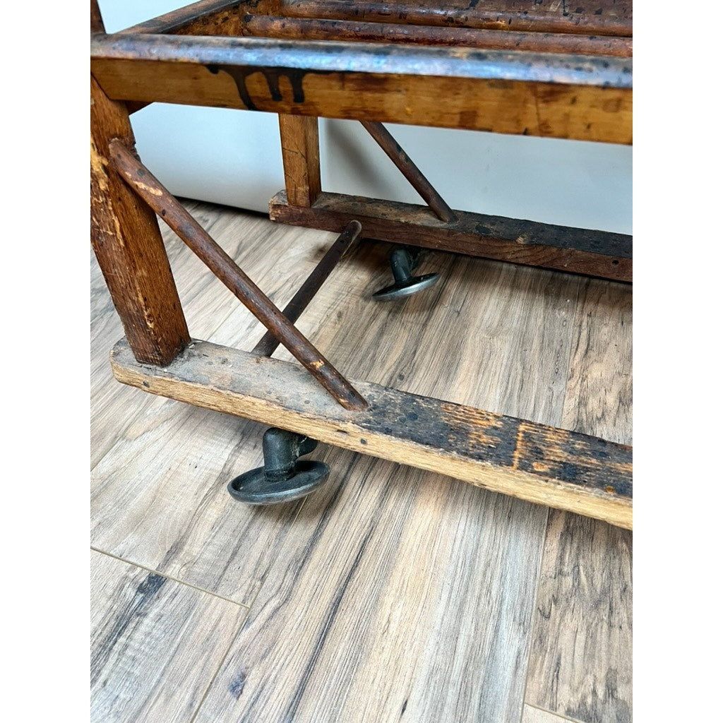 A close-up of the Antique Oak Shoe Factory Rolling Rack from the late 19th century, showing visible wear and original industrial casters, resting on a light wood floor.