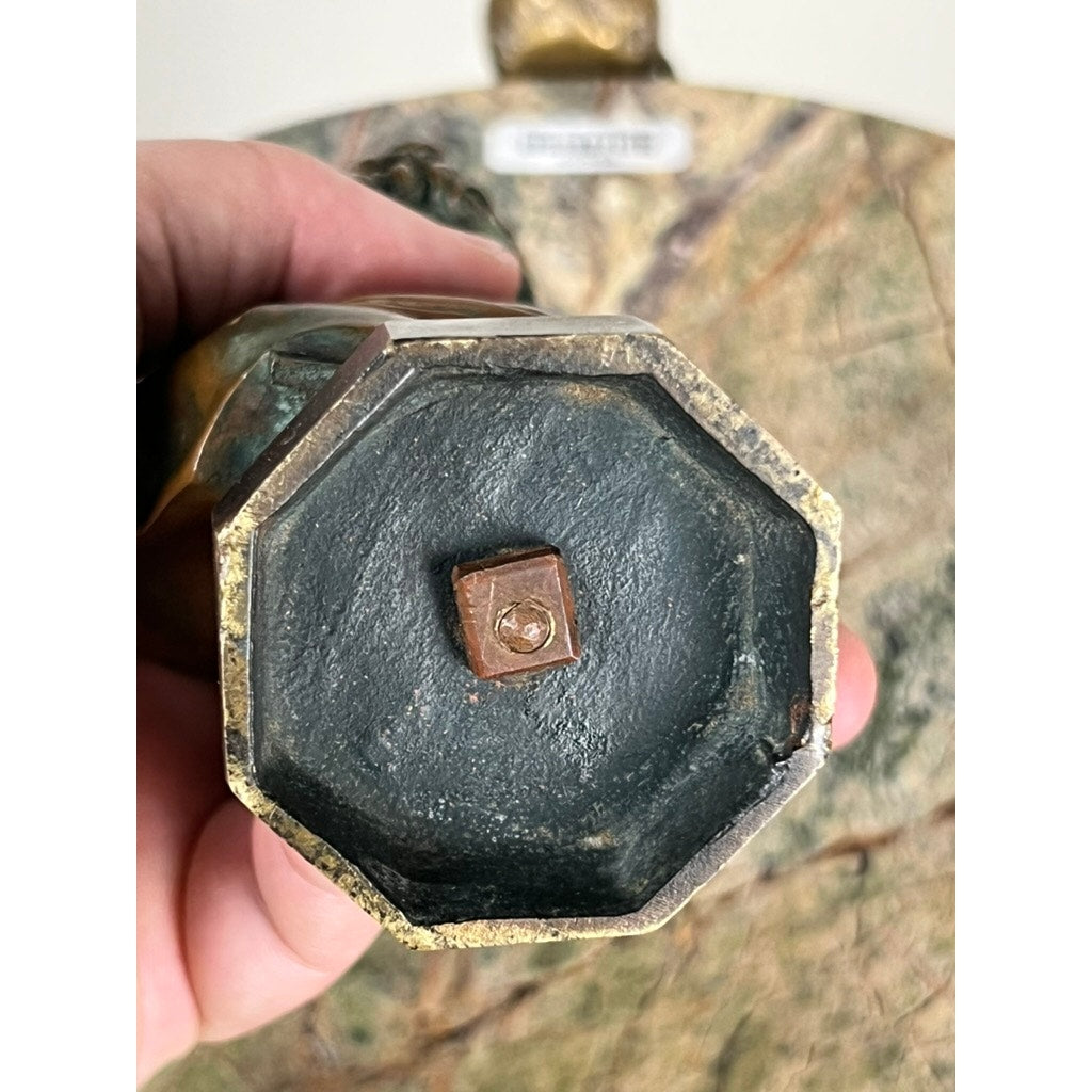 A close-up of the base of an Antique Small Bronze of “the Apollo Belvedere” with Vienna Foundry Mark, showing its octagonal bottom and central rusted screw, held in hand over a stone background. Brand: Unknown.