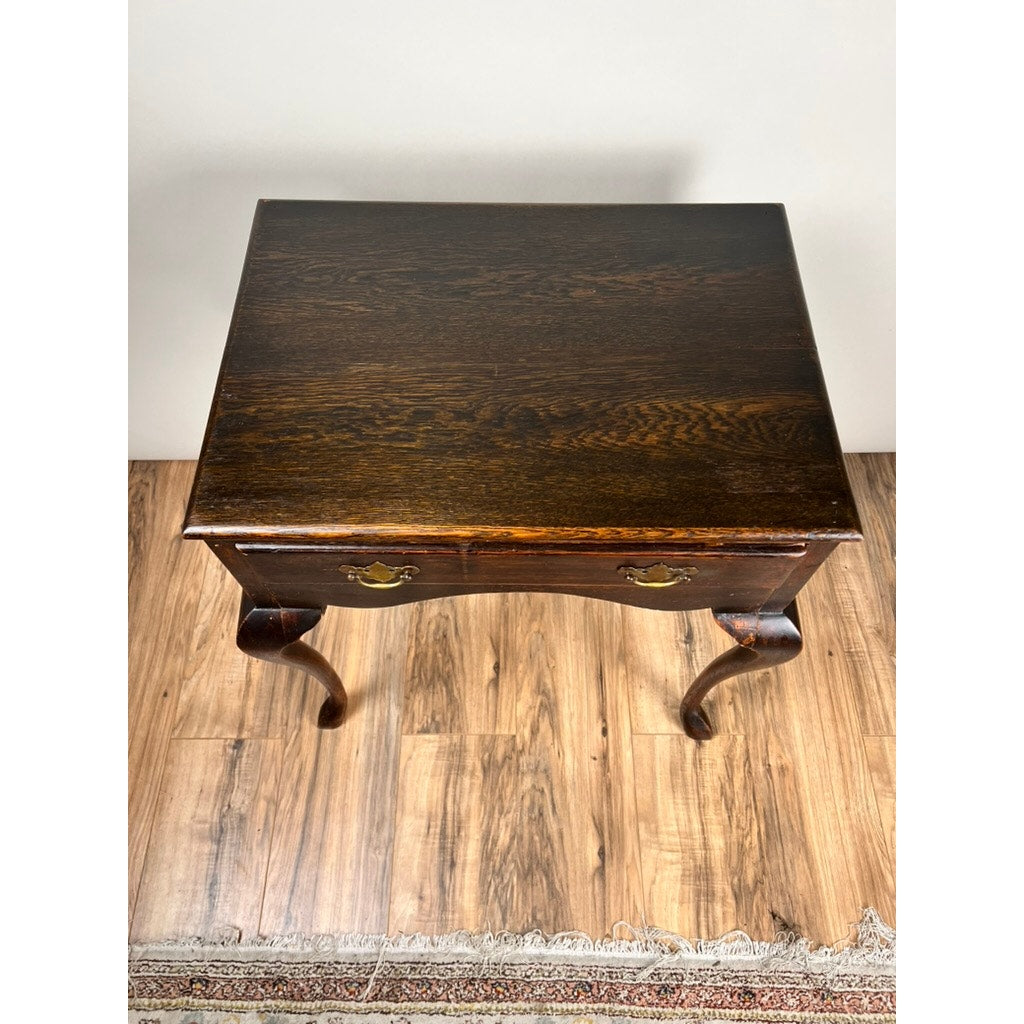 An Antique Queen Anne Style George III Oak One Drawer Stand, late 18th century, stands on a wooden floor by the edge of a woven rug.