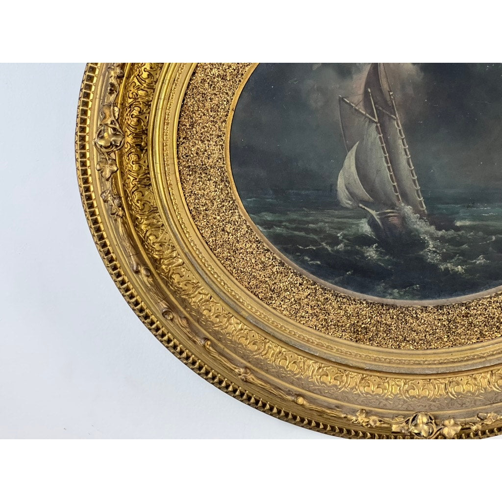 A close-up of the Antique Oval “Storm Tossed Ship” Oil on Board Painting (Late 19th Century) shows a sailboat braving rough seas beneath cloudy skies, set in an ornate gilt frame with intricate raised patterns. Brand: Unknown.