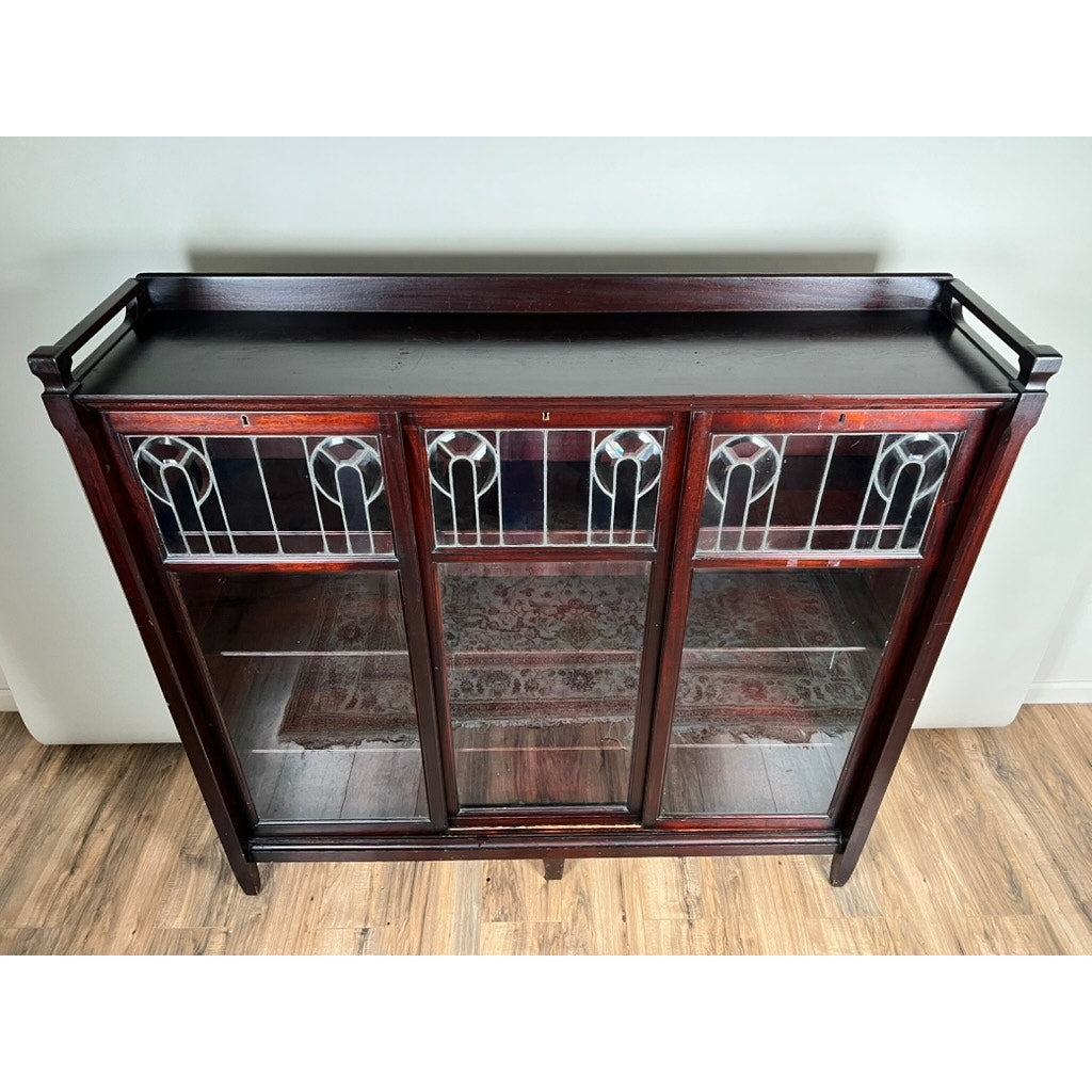 The Antique Arts & Crafts Leaded Glass Mahogany Bookcase c. 1920 features three glass doors with decorative leaded panels, exemplifying classic bookcase style and elegance.