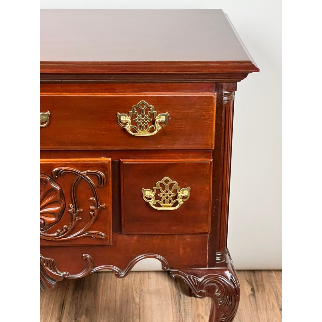 A close-up of the Vintage Solid Mahogany Chippendale Style Lowboy by Councill Craftsmen, featuring ornate carving and brass handles on a wood floor, highlights the brand’s signature elegance against a light background.