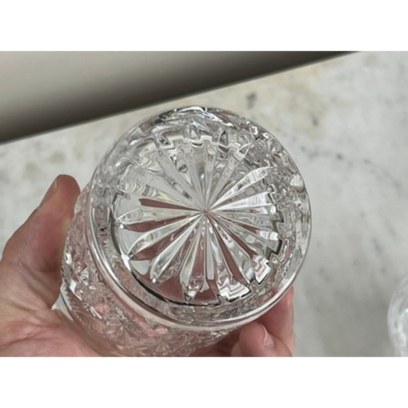 A hand holds a clear Fostoria Stowe Double Old Fashioned Tumbler, seen from above to highlight the starburst base pattern—an elegant vintage-inspired detail. The background is a light, subtly textured surface. Sold as a pair.