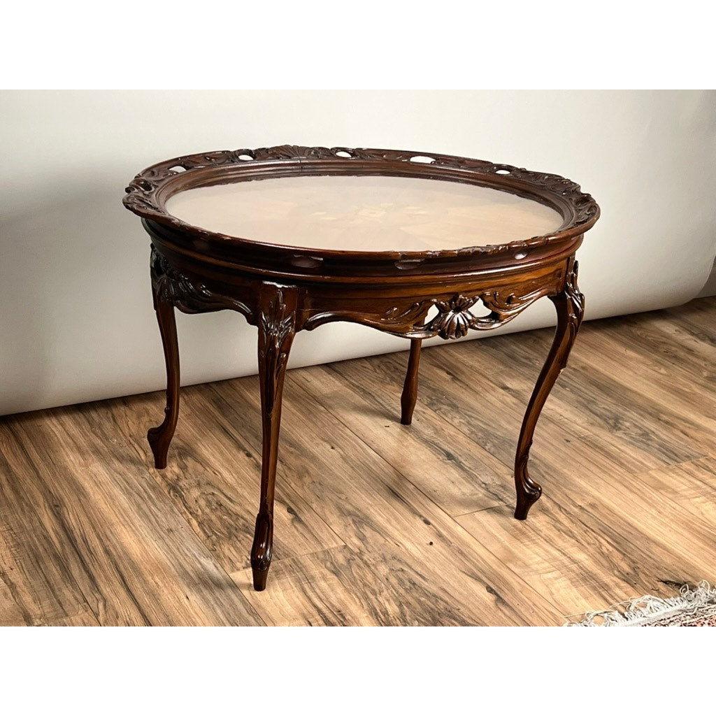 The Vintage Louis XVI Style Butlers Table with Removable Glass Tray features ornate carved details, curved legs, and a polished brown finish, displayed on a wooden floor against a neutral background.