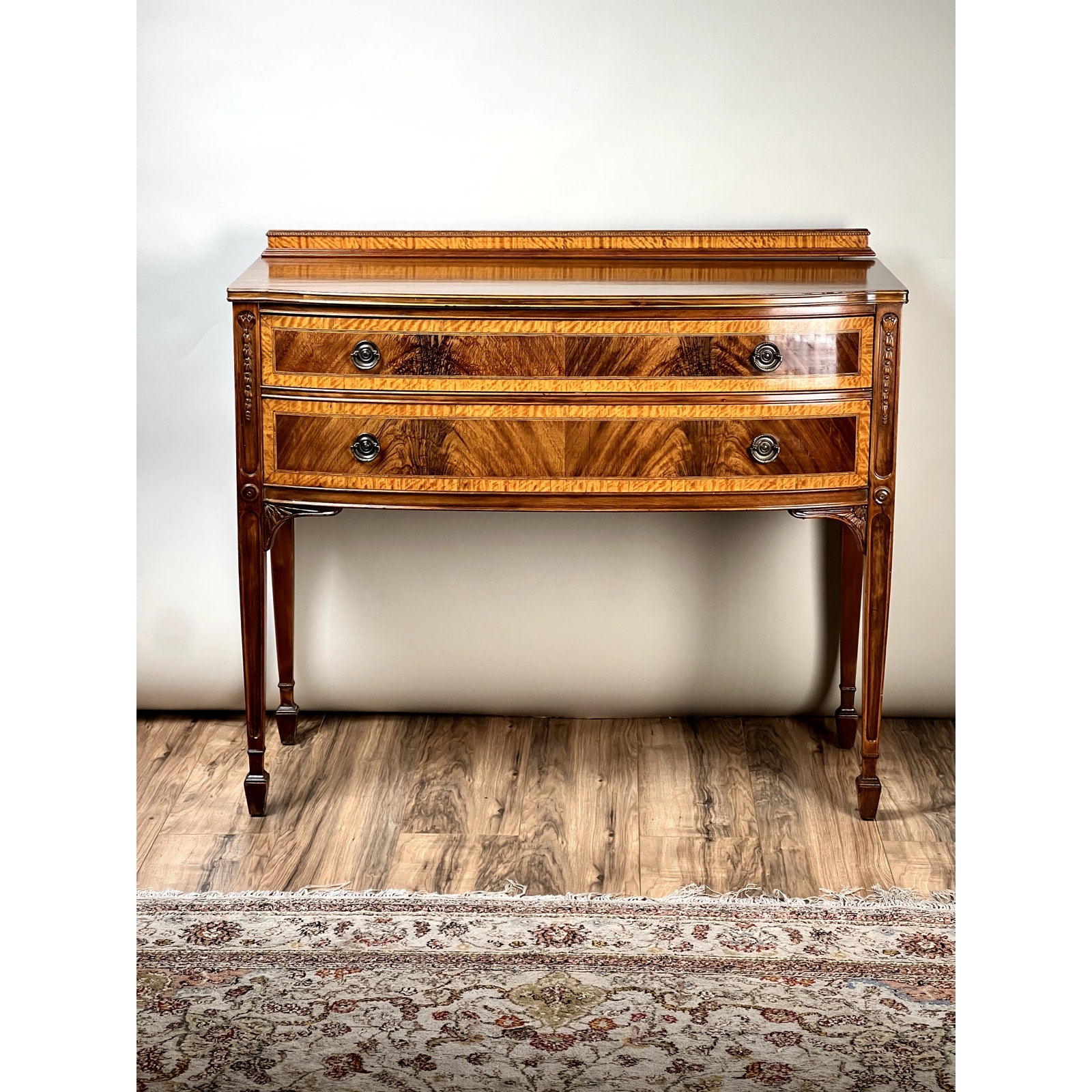 Vintage Federal Style Bow Front Mahogany Sideboard by Paine Furniture Boston featuring two drawers with ornate metal handles, tapered legs, and a rich glossy finish, shown on a wooden floor with a patterned rug.