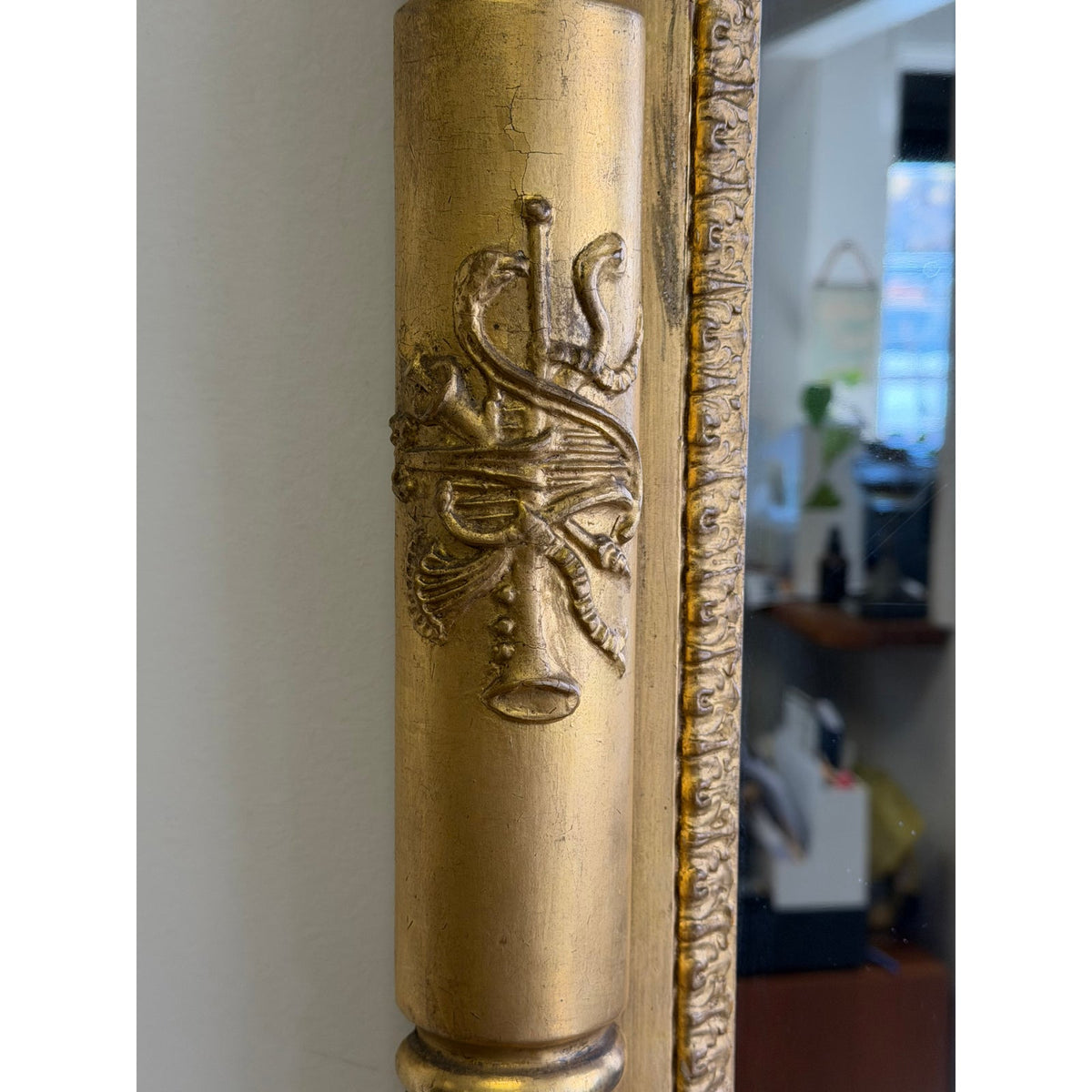 Close-up of an American Federal Giltwood Pier Mirror, possibly Massachusetts or New York, circa 1815–1830, featuring a gold-toned frame with a relief carving of a caduceus and a musical instrument.