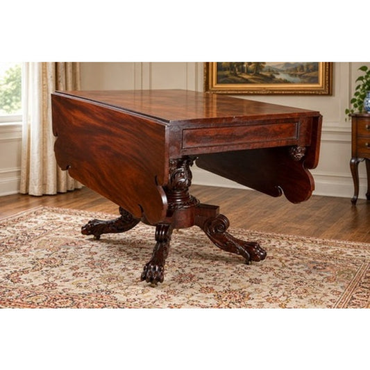 An American Classical Carved Mahogany Drop-Leaf Breakfast Table, c. 1825–1840, featuring a central pedestal base with ornate carvings and claw-and-ball feet.