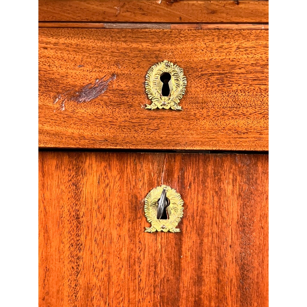 Close-up of two ornate brass keyholes—one missing a cover, the other partially closed—on an Antique French Empire Secrétaire Abattant with ormolu mounts, crafted in rich mahogany veneer, c. mid 19th century.