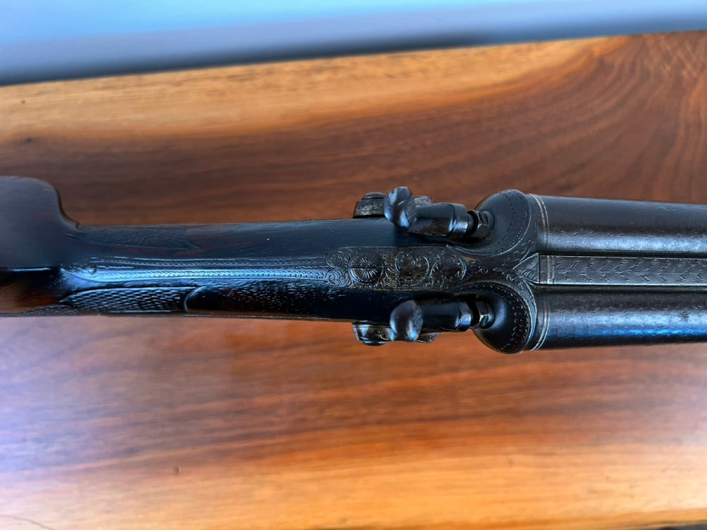 Close-up of an Antique Christoph Funke Suhl German Damascus Double Barrel Hammer Shotgun, c. 1880, featuring intricate metal engravings and stunning Damascus barrels with a carved stock, resting on a wooden surface—a true testament to the craftsmanship offered by Pearl City Antiques.
