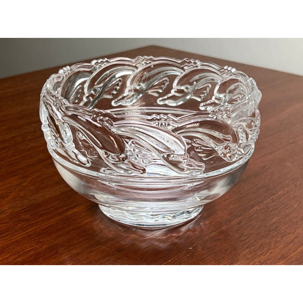 A Vintage Tiffany & Co. Mid-Century Modern Crystal Dolphin Pattern Footed Bowl sits elegantly on a polished wooden surface, its clear glass adorned with the iconic dolphin motif along the rim.