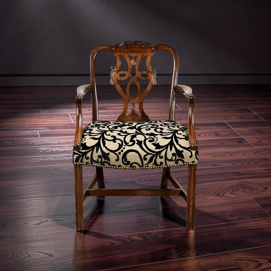 An Antique George III Chippendale Open Arm Chair from the early 19th century, featuring an ornate carved backrest and cream upholstery with a black floral pattern, sits on a polished dark wood floor against a plain dark background.