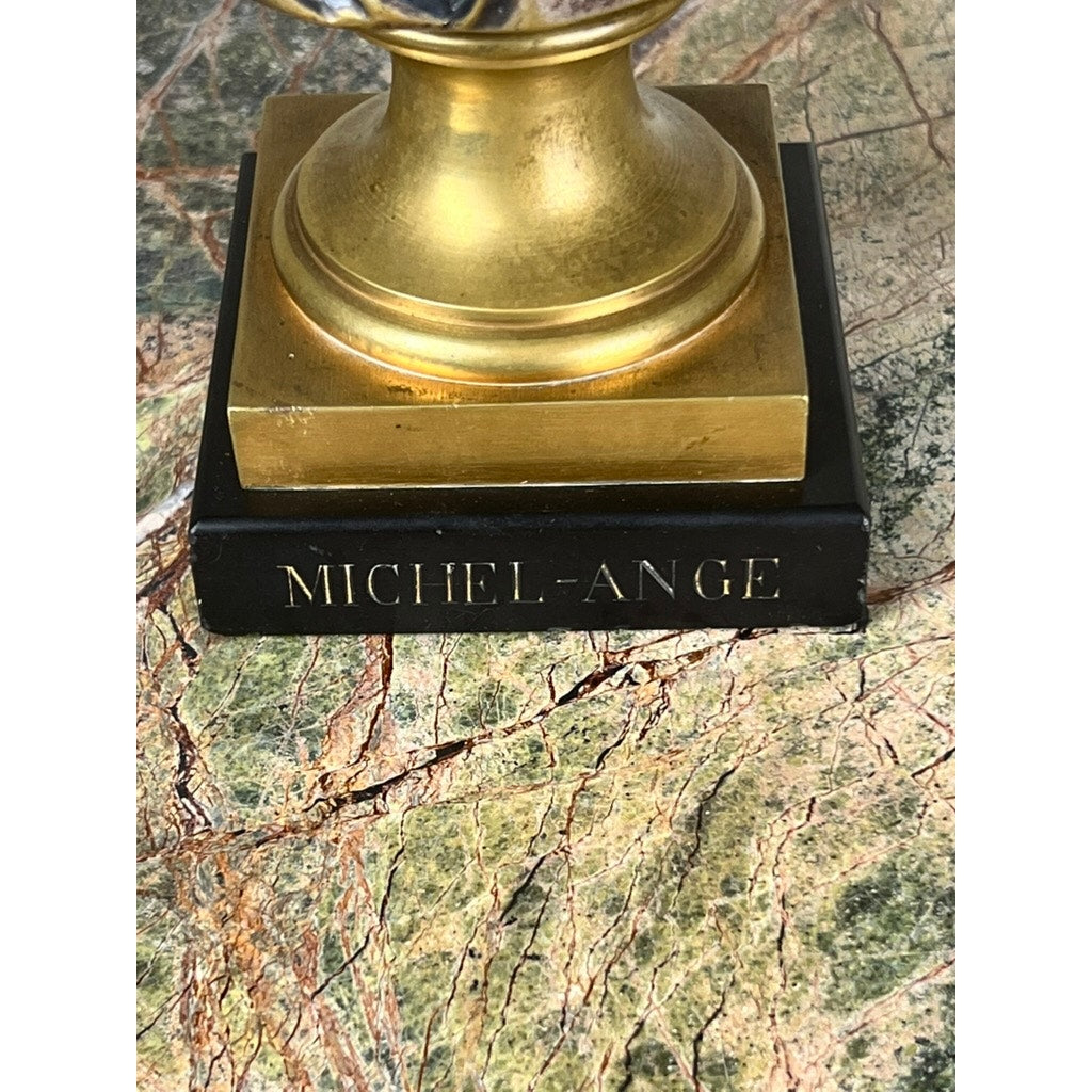 A close-up of a patinated bronze sculpture of Michelangelo by Albert-Ernest Carrier-Belleuse, modeled before 1883 in Paris, features a gold statue base on marble and a black plaque engraved with "MICHEL-ANGE.