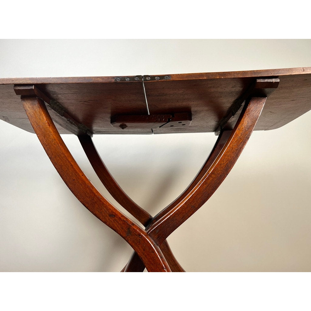 Close-up of the underside of an Antique English Regency Mahogany Folding Coaching or Sporting Table (c. 1825–1845), showing its curved legs and metal hinges, set against a plain light background.
