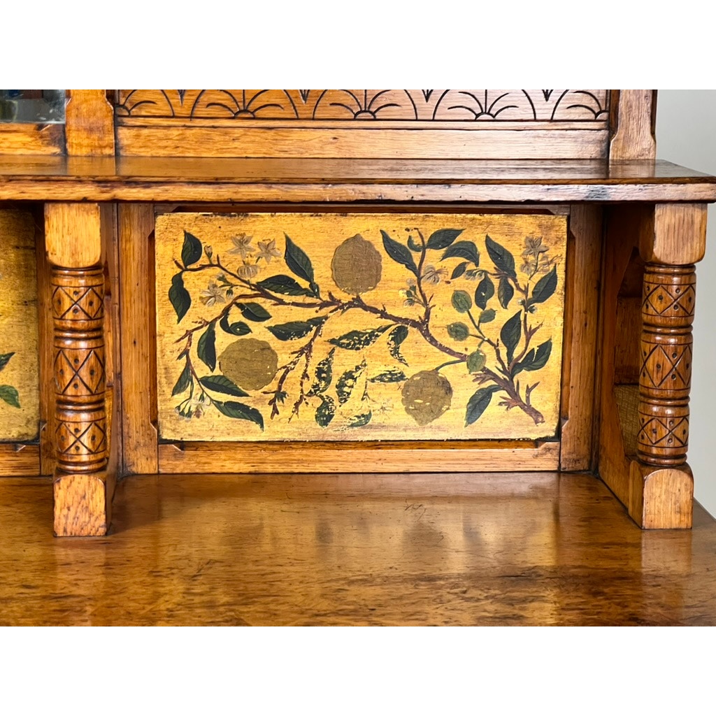 Close-up of an Antique Victorian Aesthetic Movement Oak Desk in Original Finish, c. late 19th century, showcasing carved columns and a hand-painted panel with green leaves, branches, and fruit on yellow. Polished wood radiates elegance.