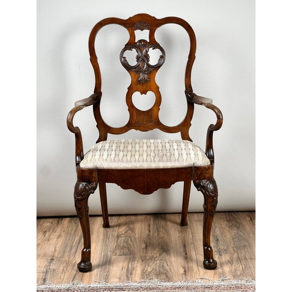 An Antique George III Mahogany Open Arm Chair c. Late 18th Century, featuring ornate carvings and a light patterned upholstered seat, is shown on a wooden floor against a plain white wall. Brand: None/Unknown.