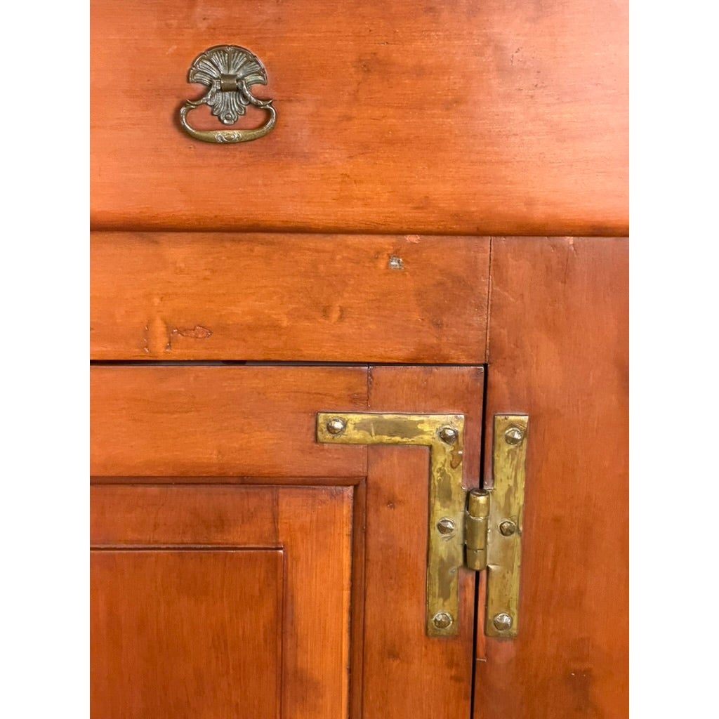 Close-up of a Pennsylvania or Mid-Atlantic Cherry Open Pewter Cupboard, circa 1800–1830, featuring a brass drawer pull with a floral design and an L-shaped brass hinge on the door.