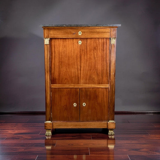 An Antique French Empire Secrétaire Abattant with Ormolu Mounts by Pearl City Antiques, dating from the mid-19th century, stands tall against a plain dark background on a polished wooden floor. This elegant piece features claw feet, a luxurious mahogany veneer, a marble top, and multiple keyhole locks.