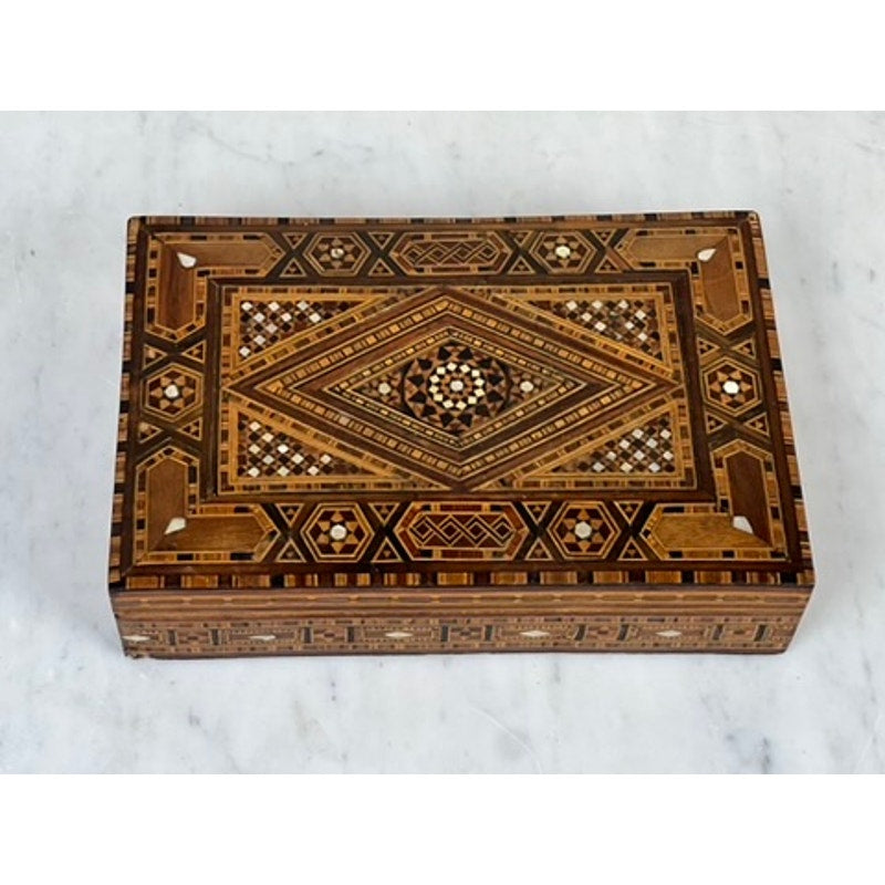 An Antique Persian (likely Syrian) Khatam wood inlaid jewelry box, early 20th century, with intricate geometric brown, cream, and black designs rests on a white marble surface. Brand: None/Unknown.