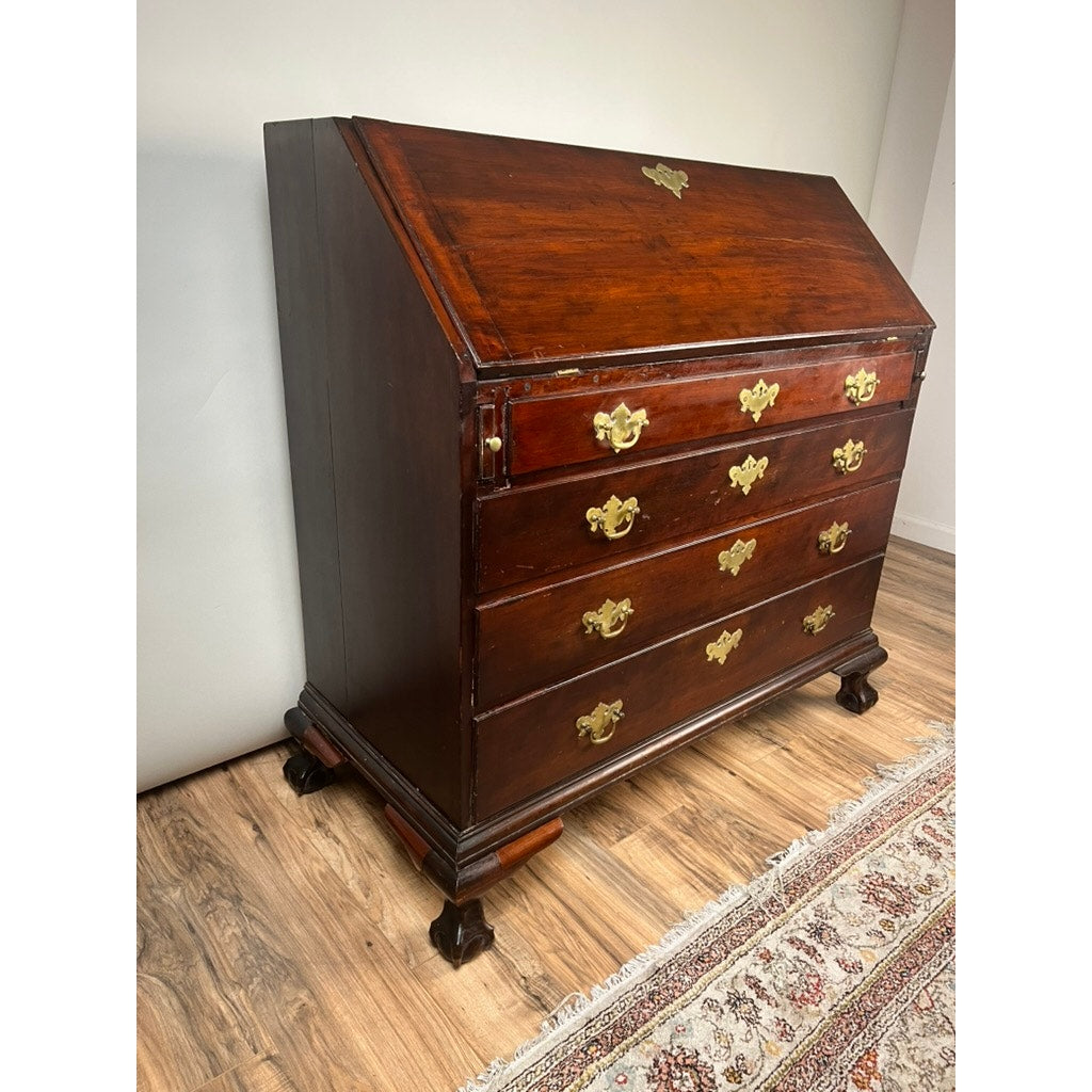 The 18th Century New England Chippendale Cherry Slant Front Desk, circa 1770–1790, is crafted from solid cherry and features four drawers with brass handles, elegant claw feet, and a distinctive slant-front top. This refined antique provides a stunning focal point above a decorative rug partially visible on the wooden floor.