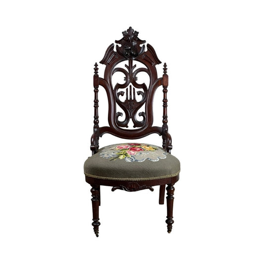 Antique Victorian Rococo Revival carved walnut slipper chair, late 19th century, featuring an ornate backrest, turned legs, and a floral needlepoint upholstered seat. Brand unknown.