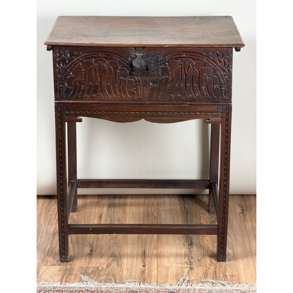 English Jacobean Carved Oak Bible Box on Later Stand from Pearl City Antiques, featuring a 17th-century oak box with a carved front panel and metal latch, resting on a matching wooden stand with four straight legs.