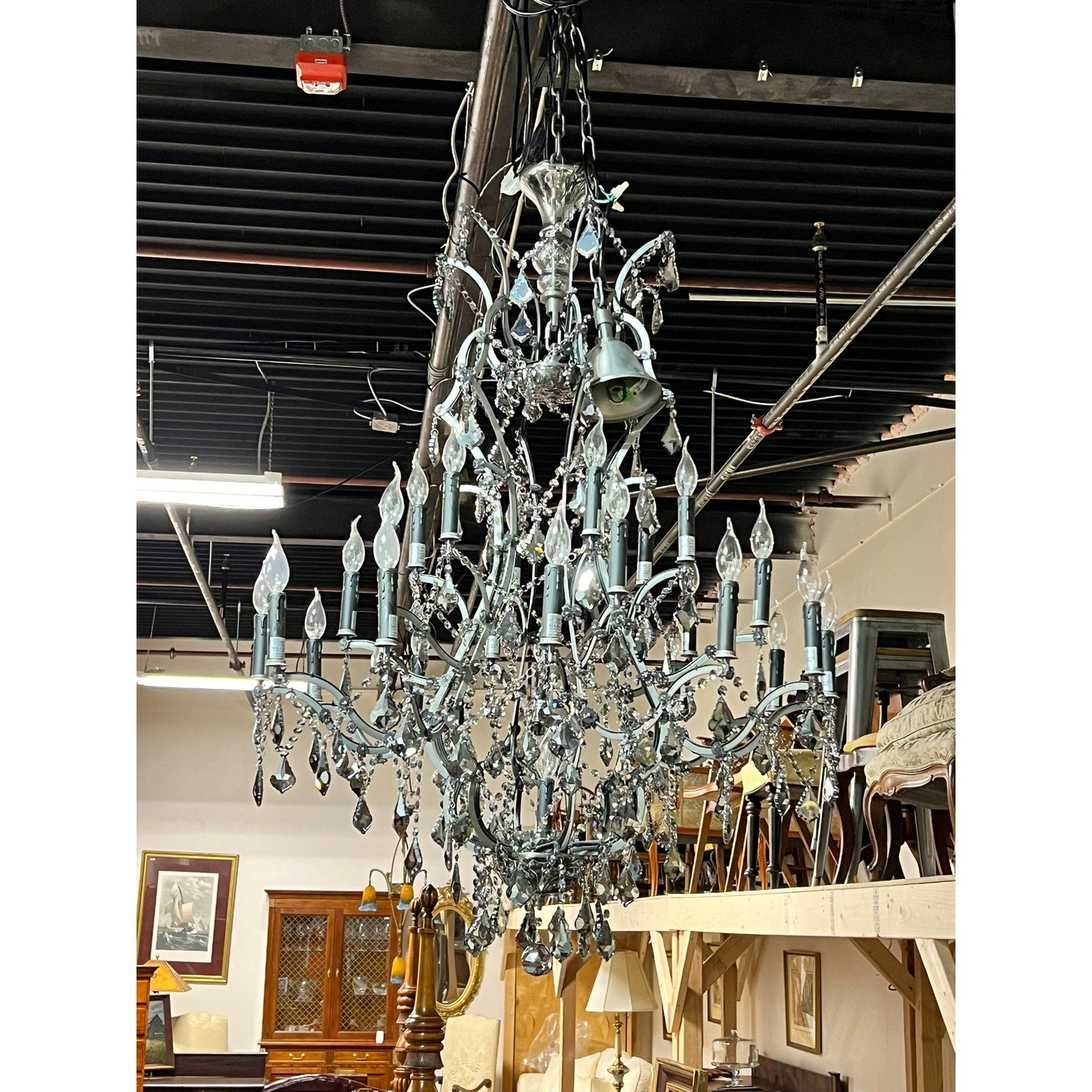 A Large Vintage Smoke Crystal 24 Light Chandelier hangs from a high ceiling, illuminating a room adorned with antique furniture and artwork.
