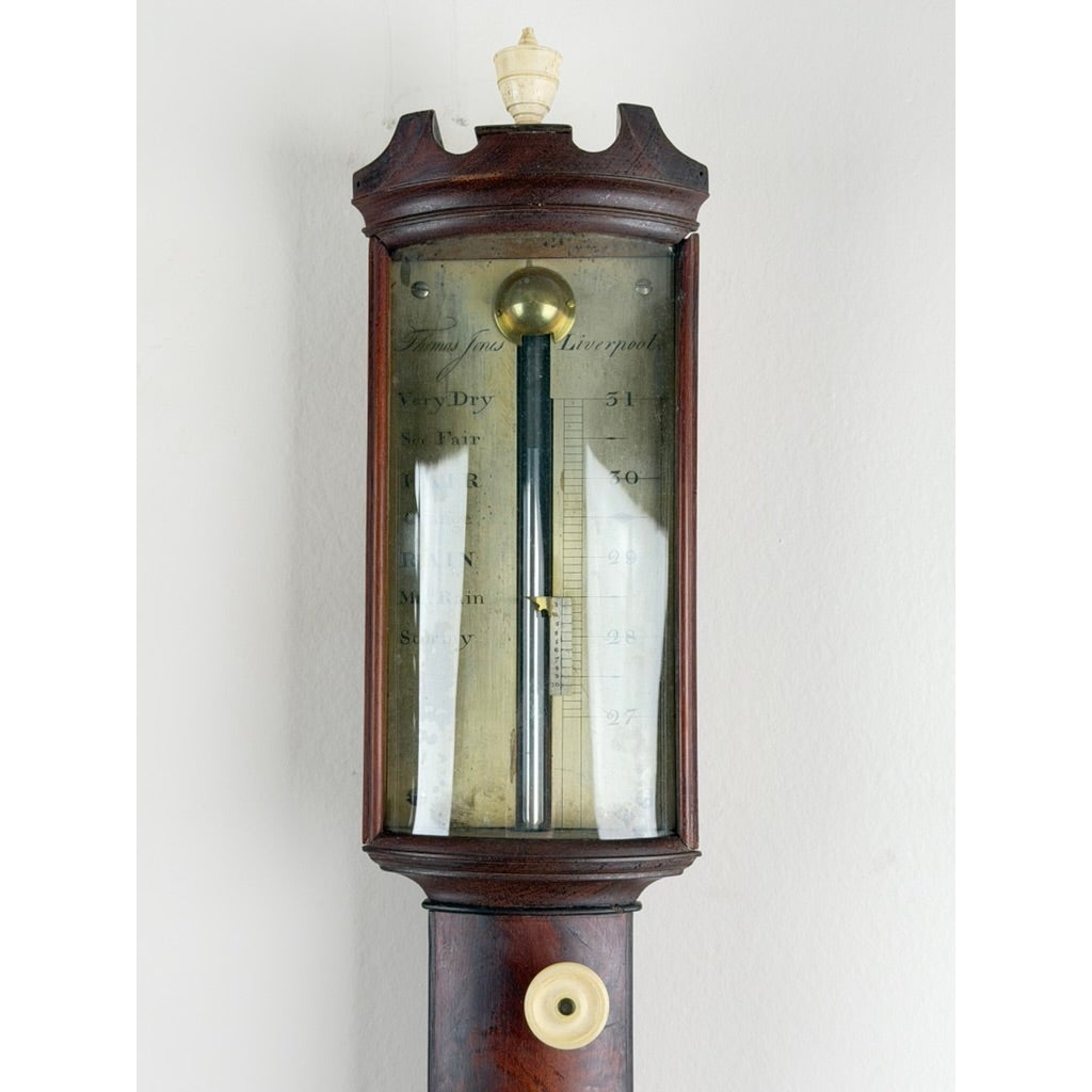 English Regency mahogany stick barometer by Thomas Jones, featuring a brass reservoir and a glass-enclosed gauge with weather notations and a numbered scale.