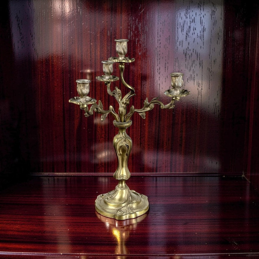 A Vintage Brass Louis XV Style Four Light Candelabra, of unknown brand, sits on a polished dark wood surface, its brass gleaming under the light.
