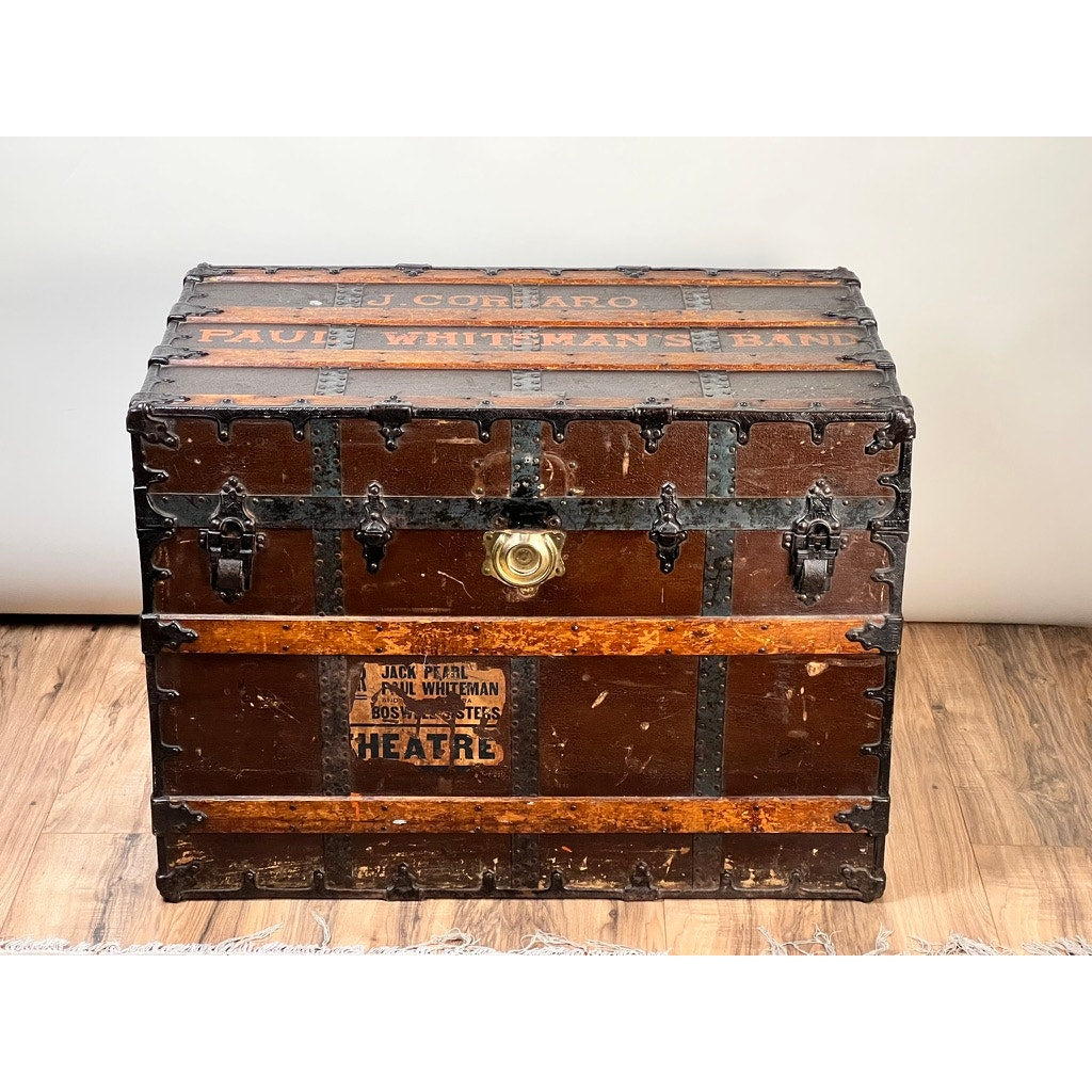 A c. 1930s CA Taylor Touring Trunk of John B. Cordaro, Paul Whiteman Orchestra reed player, features metal reinforcements and a brass lock—its faded lettering reflects a storied big band music past, displayed on a wooden floor.