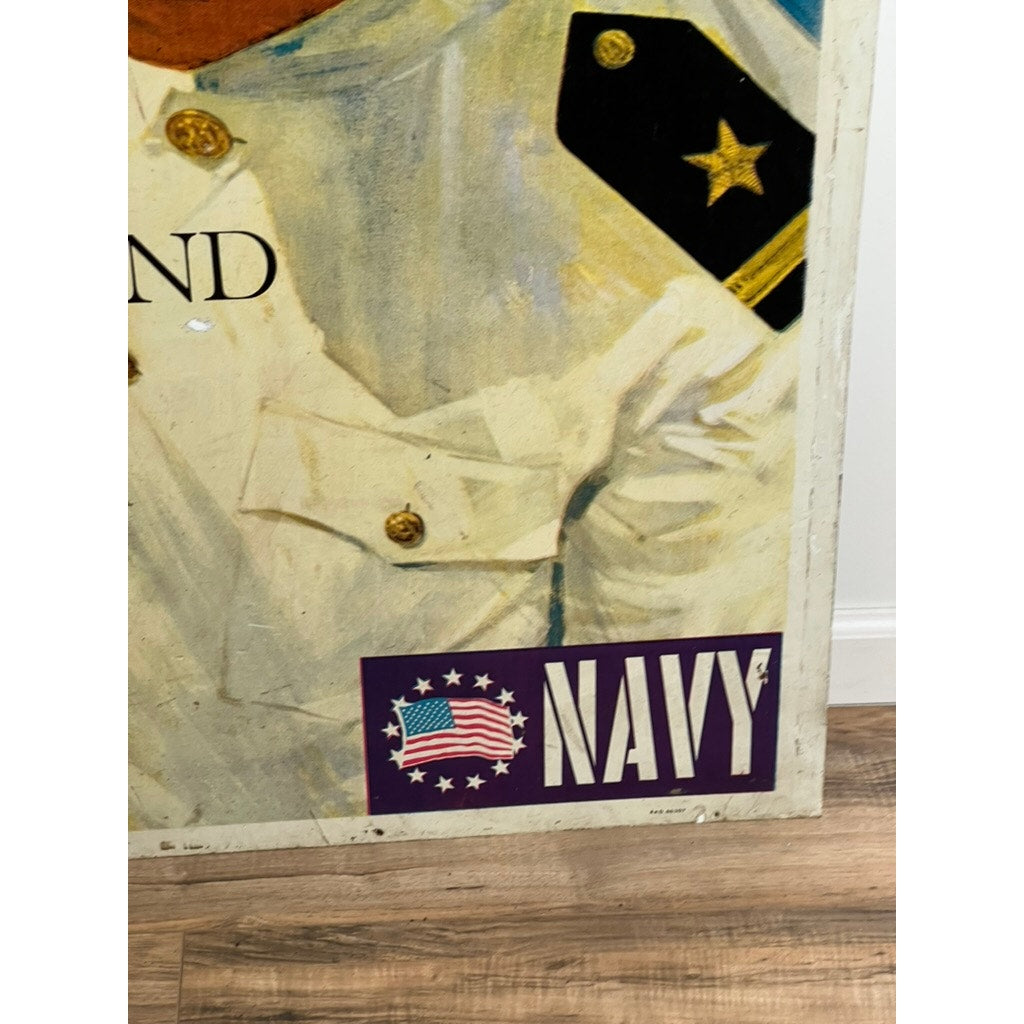 A close-up of an original Vietnam Era double-sided U.S. Navy recruiting tin sign by artist Lou Nolan features part of a white-uniformed figure and NAVY label near a flag emblem, promoting the USS Saratoga; the collectible rests on a wooden floor.
