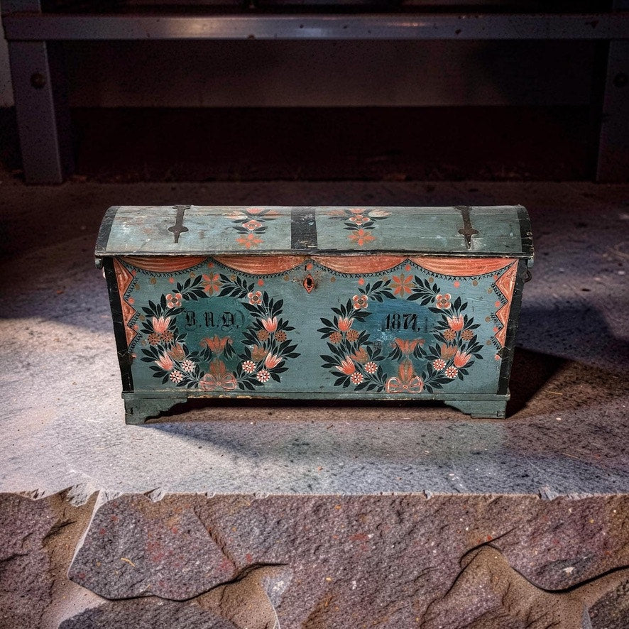 An Antique Swedish Oak Kista Dowry Chest c. 1841 sits on a rough stone floor in a dimly lit room—a striking example of Swedish folk art with ornate green paint and floral patterns. Brand: None/Unknown.