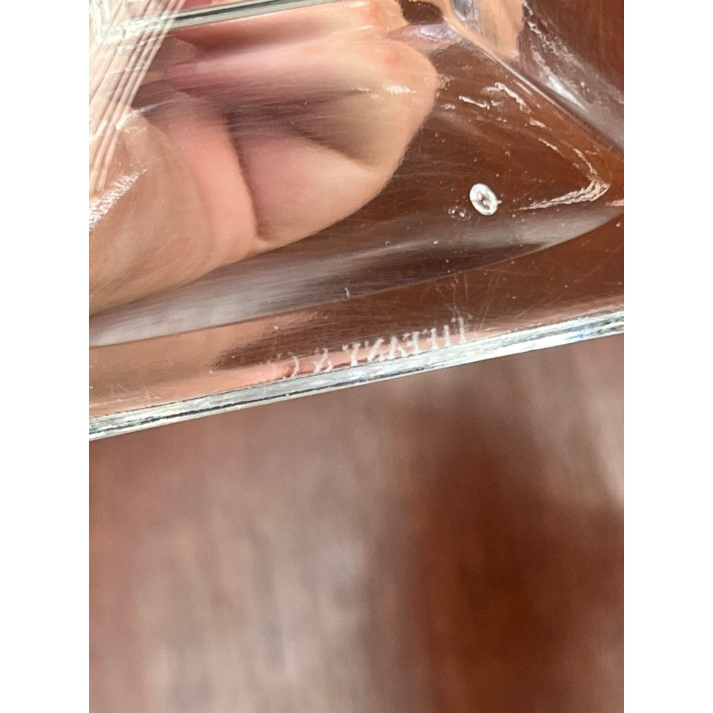 Close-up of a hand holding a Vintage Pair Tiffany & Co Clear Crystal Candlestick, engraved with TIFFANY & CO., set against a wood-grain background.