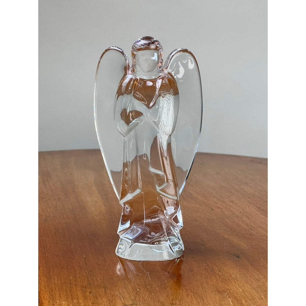 The Vintage Baccarat Crystal Angel by Baccarat, featuring delicate wings, stands on a wooden surface against a plain, light-colored background.