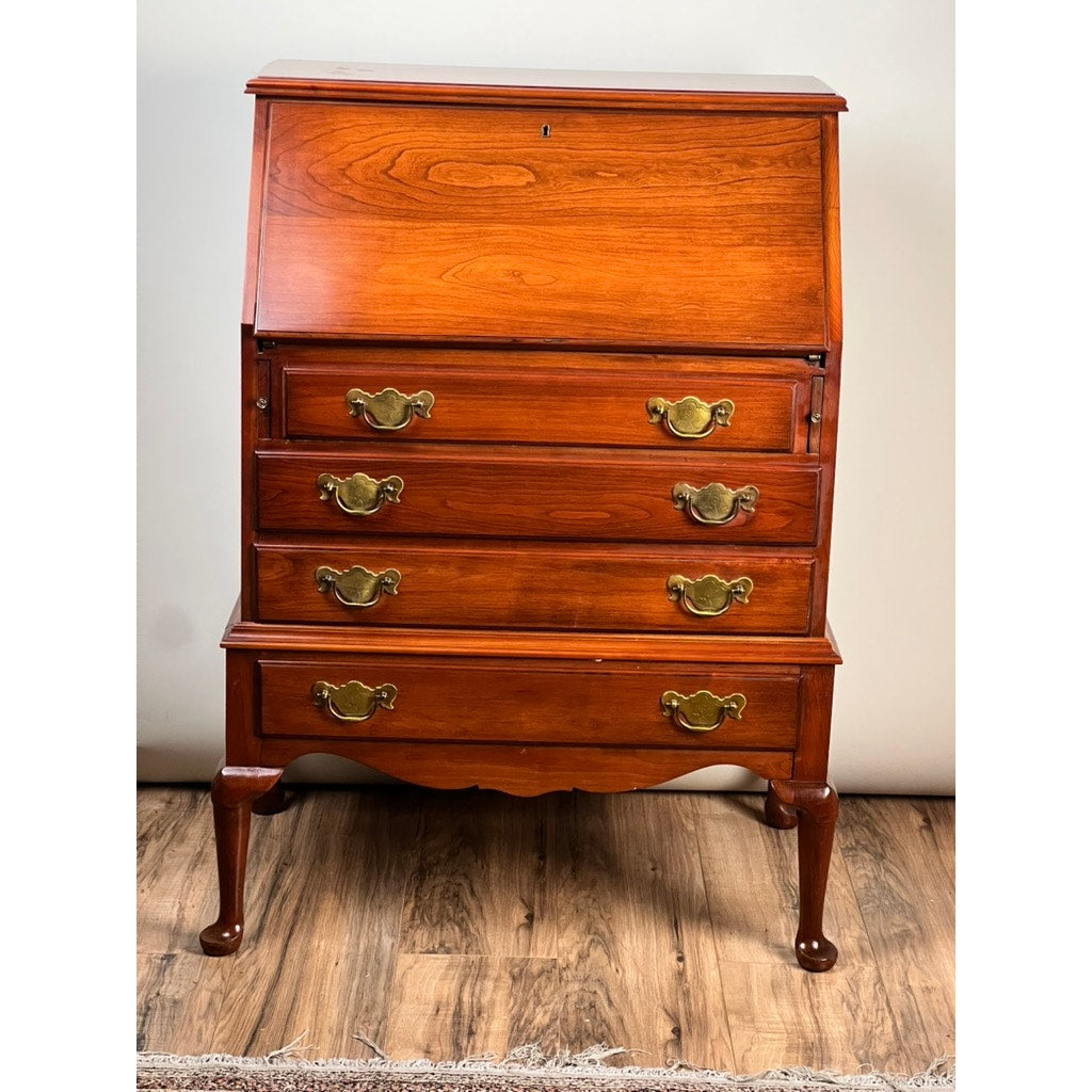 A Vintage Solid Cherry Queen Anne Style Slant Front Secretary Desk by Pennsylvania House, featuring four brass-handled drawers and short curved legs, stands on a wood floor against a plain light wall.