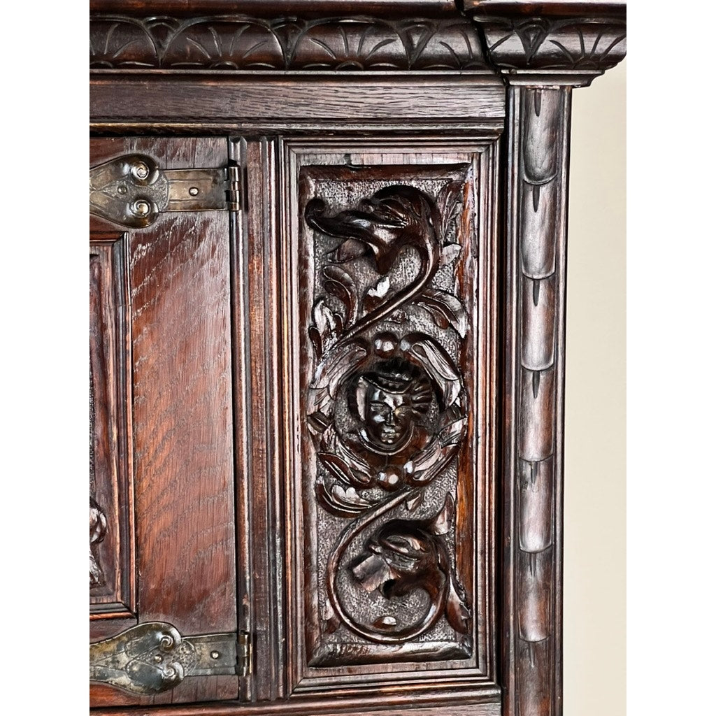 Close-up of an Antique 19th-Century French Breton-style carved oak cabinet door, featuring deeply carved knights, ornate floral and leafy motifs, and decorative metal hinges. Brand: unknown.