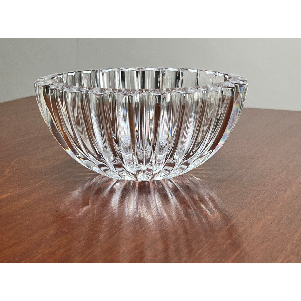A Vintage Tiffany & Co. Crystal Bowl in a ribbed petal design sits on a polished wooden surface, its clear facets casting light reflections—a stunning centerpiece from Tiffany & Co.