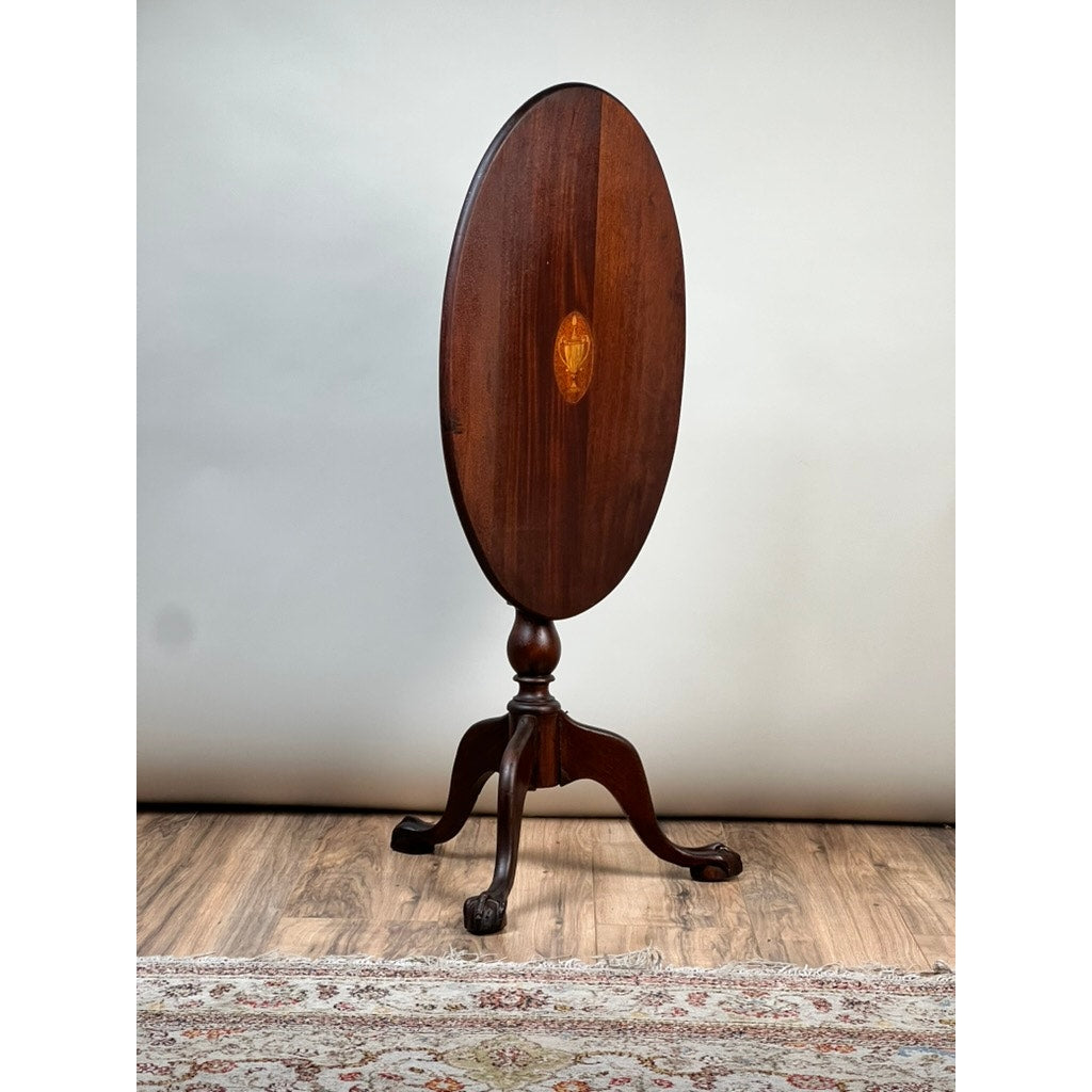 Antique George III Tilt-top Tea Table c. Early 19th Century by Pearl City Antiques, featuring an oval tilt-top surface, pedestal base, and three gracefully curved legs, displayed on a wood floor next to a patterned rug and set against a plain light background.