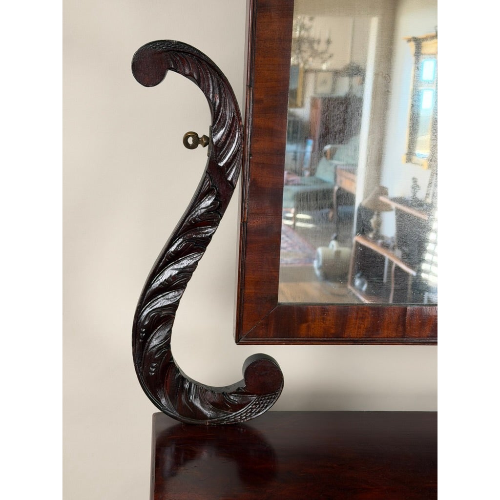An American Classical Carved Mahogany Dressing Table with Original Mirror, featuring a dark wood finish and a large, ornate S-shaped carved support for the vanity mirror.