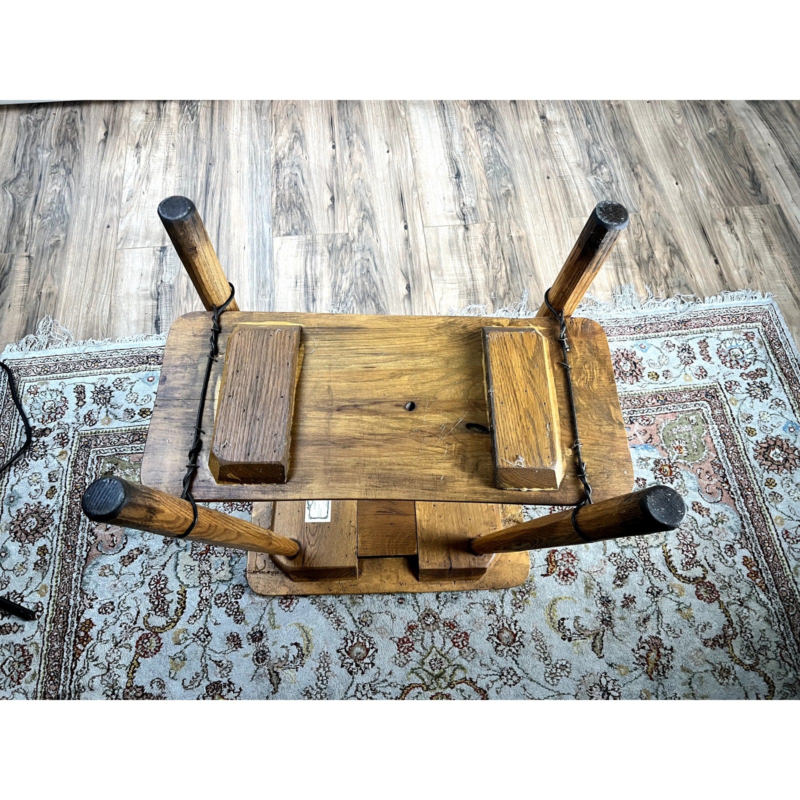 The Vintage Wabi Sabi Bench from Spalted Maple, signed Neil Panyik, is shown upside down on a patterned rug, highlighting its unique wood grain and sturdy legs. A wood floor and part of an ornate carpet are visible in the room.