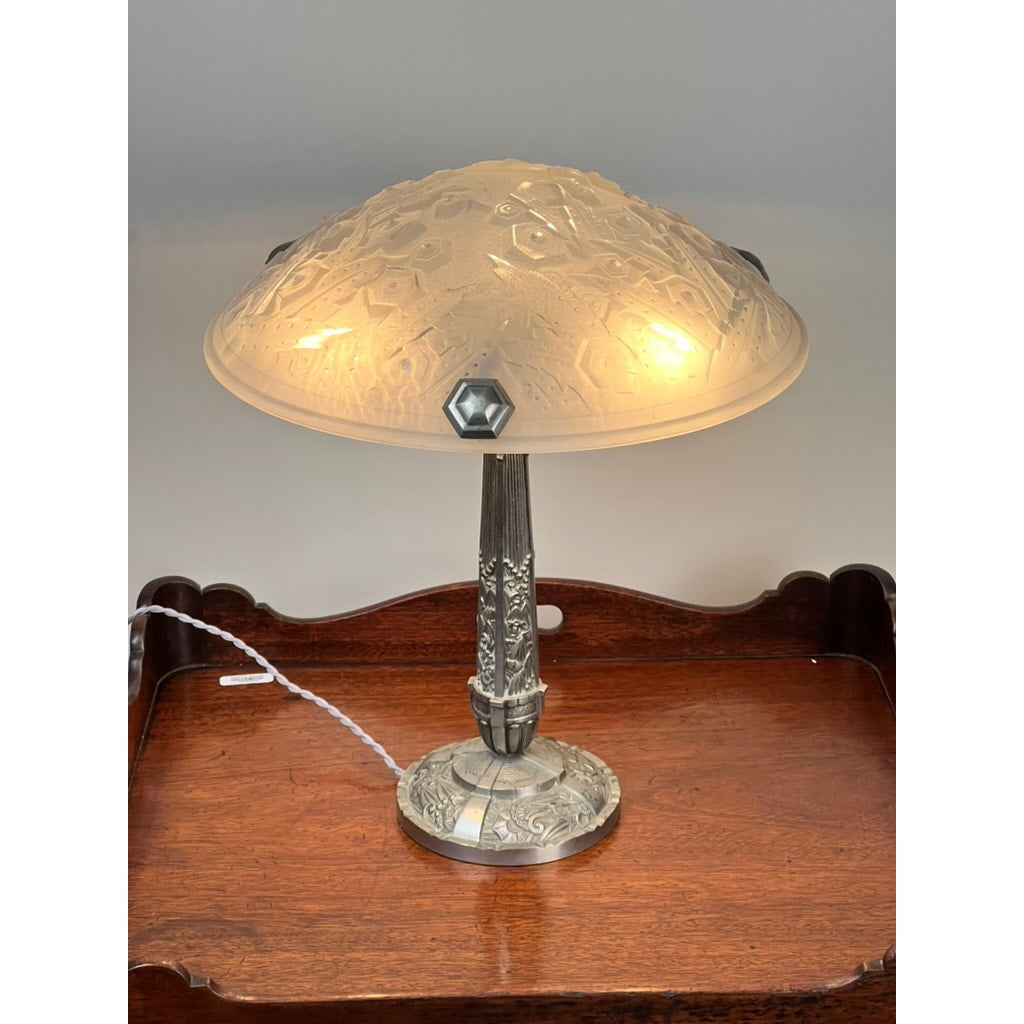 Vintage French Art Deco Frosted Glass Table Lamp by Muller Frères Lunéville c. 1920, with ornate frosted glass shade and detailed metal base, illuminated on a polished wooden table against a plain background. Brand: None/Unknown.