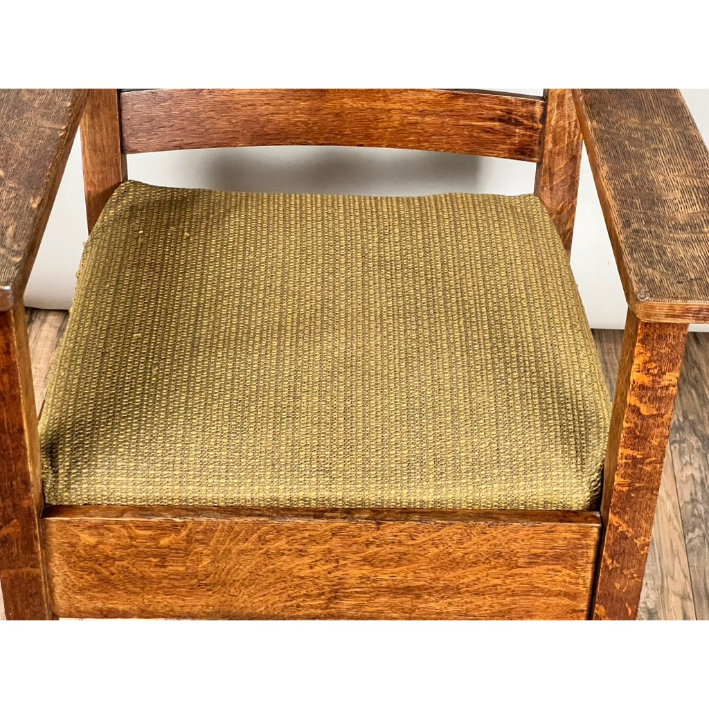 An Antique Quarter Sawn Mission Oak Arm Chair by Quaint Furniture (c. 1920) with square arms and olive-green textured upholstery, shown on a wooden floor against a plain white background.